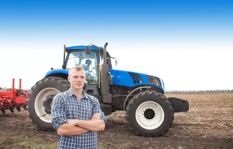 A young farmer standing proudly in front of the new tractor he purchased thanks to a loan from OUCU.